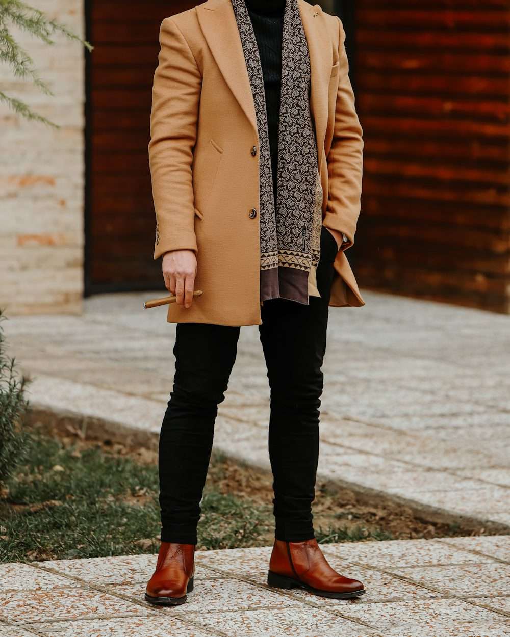 Un uomo con cappotto color cammello, sciarpa stampata, dolcevita nero e stivaletti in cuoio