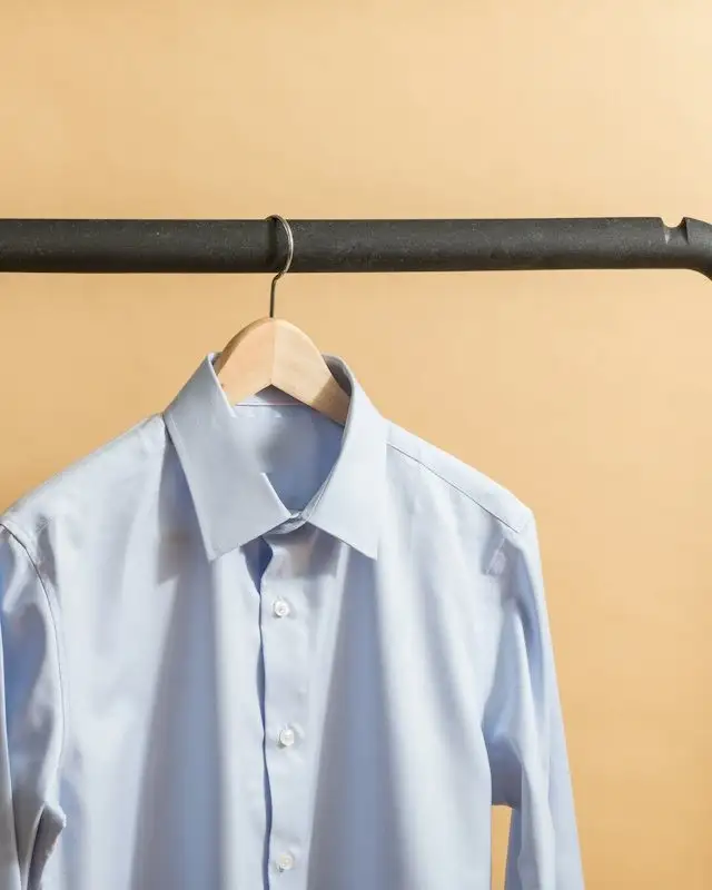Camicia azzurra su una gruccia di legno appesa a una barra di ferro