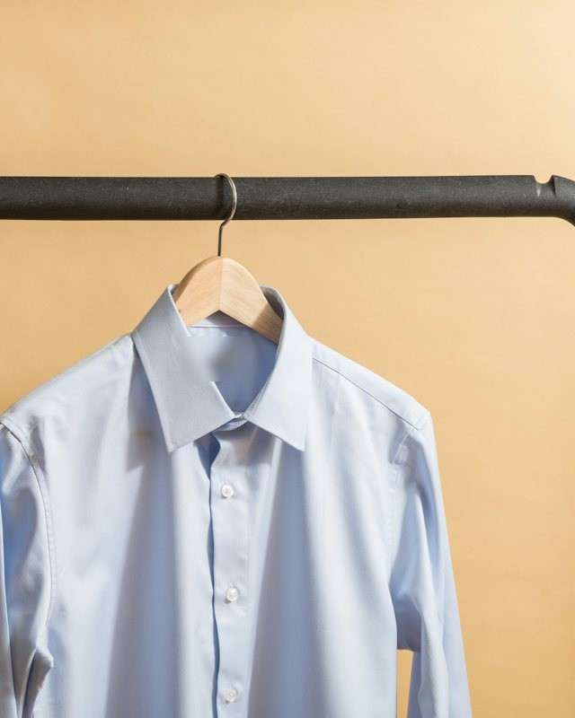 Camicia azzurra su una gruccia di legno appesa a una barra di ferro