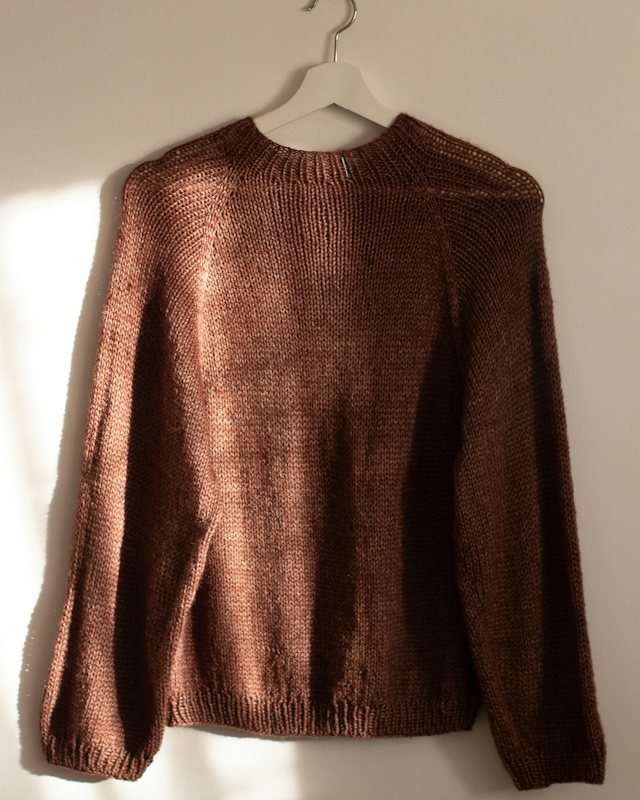 Maglia girocollo color cognac appesa a una gruccia, alla luce del sole
