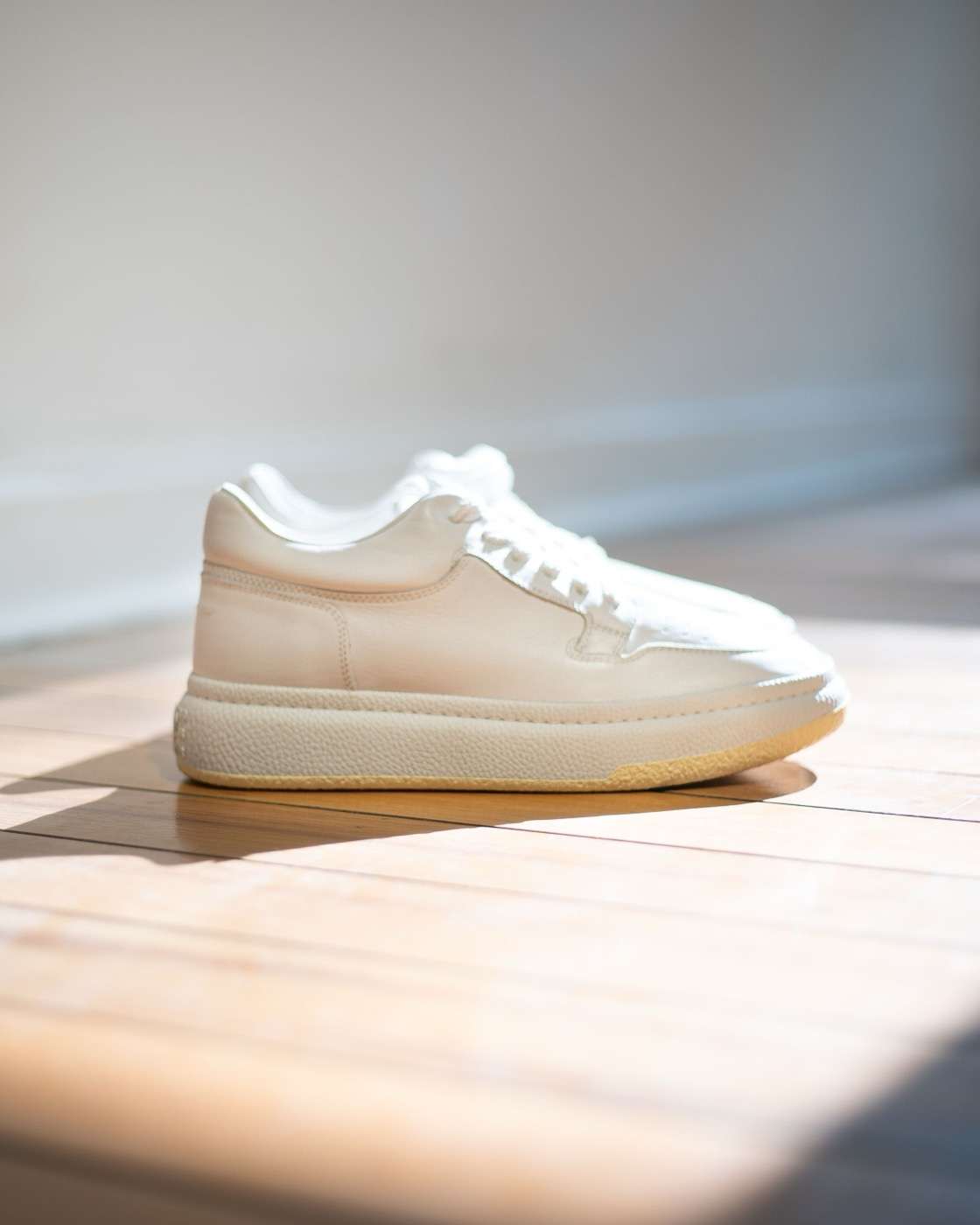 Sneaker in pelle bianca su un pavimento di legno, alla luce del sole