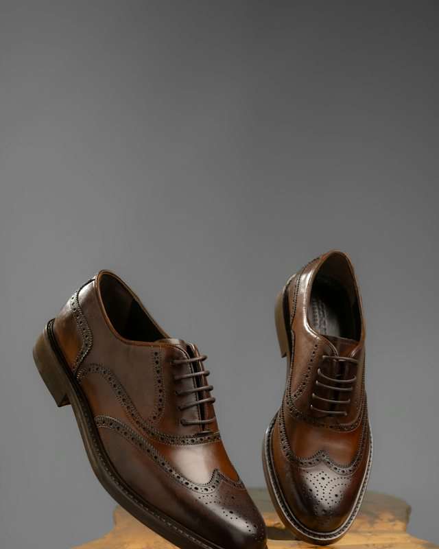 Paio di stringate brogue in pelle marrone scuro su uno sgabello di legno